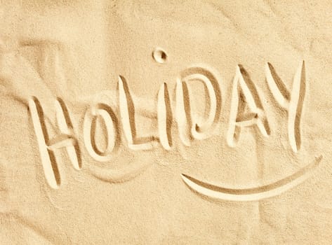The word Holiday handwritten in golden beach sand in a conceptual image of summer vacations at the seaside, tourism and travel
