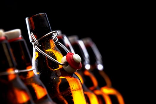 Row of glowing beer bottles with stoppers in darkness with selective focus to an opened stopper and copy space, conceptual of Oktoberfest or a brewery, pub or tavern
