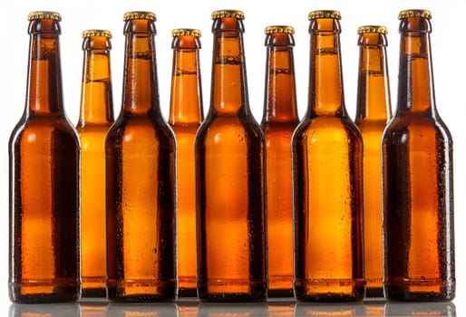 Unlabeled beer bottles standing two rows deep with metal caps and covered in condensation against a white background