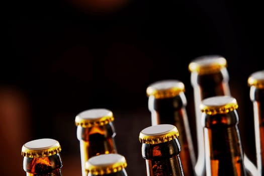 Two rows of unopened brown beer bottles in a closeup diagonal view over a dark background with copy space