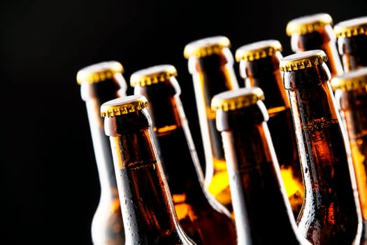 Multiple cold unopened beer bottles in a tavern or pub in a closeup view of their necks and tops over a black background conceptual of the German Oktoberfest