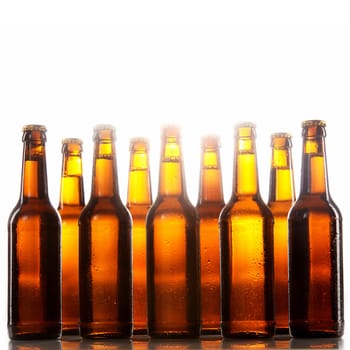 Tall beer bottles with no labels and metal caps stand two rows deep against a white background