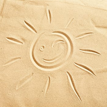 Smiling winking happy sun hand drawn on golden beach sand in a concept of tropical seaside vacations for spring and summer breaks, square format
