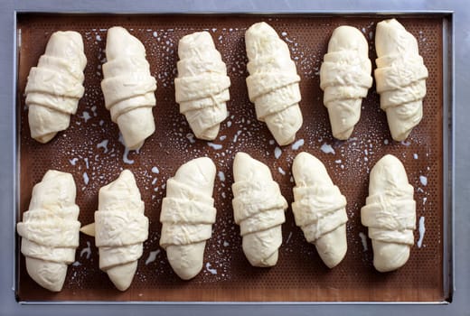 Unbaked croissant placed on brown waxed paper in a stainless steel tray