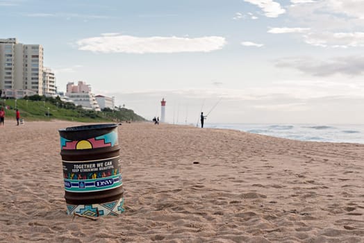 DURBAN, SOUTH AFRICA - MARCH 12, 2016: Trash can on the beach near fisherman in Umhlanga Rocks