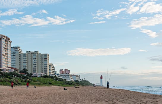 DURBAN, SOUTH AFRICA - MARCH 12, 2016: Anglers and Lifeguards on the Umhlanga Rocks beachfront with Millennium Pier and Lighthouse in the distance