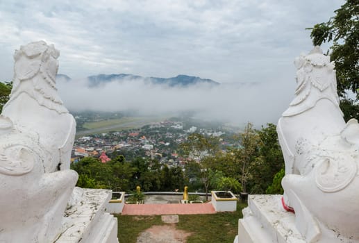 Back view of white lion statue at Wat Phra That Doi Kong Mu with aerial city view of Mae Hong Son in the mist, Thailand