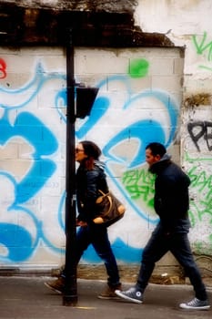 Paris,France – January 01,2014: A young couple walks past graffiti in the Arab quarter of Barbes in Paris on January 1,2014.