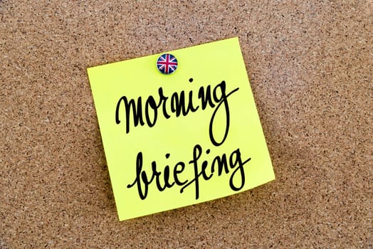 Yellow paper note pinned on cork board with Great Britain flag thumbtack, written text Morning Briefing, British Business concept