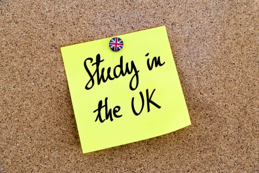 Yellow paper note pinned on cork board with Great Britain flag thumbtack, written text Study In The UK, British Business concept