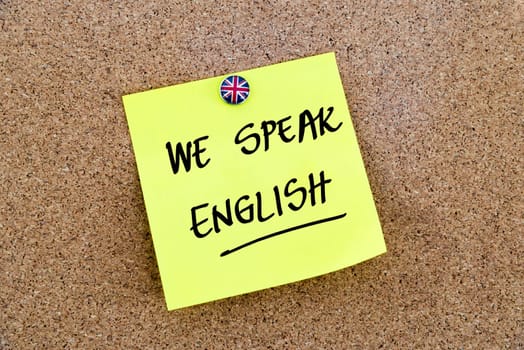 Yellow paper note pinned on cork board with Great Britain flag thumbtack, written text WE SPEAK ENGLISH, British Business concept