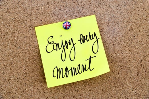 Yellow paper note pinned on cork board with Great Britain flag thumbtack, written text Enjoy Every Moment, British Business concept