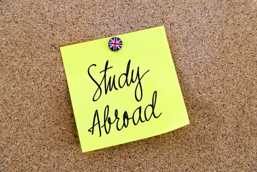 Yellow paper note pinned on cork board with Great Britain flag thumbtack, written text Study Abroad, British Business concept