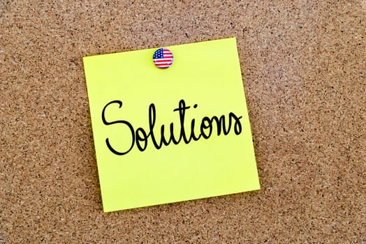 Written text Solutions over yellow paper note pinned on cork board