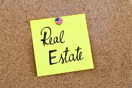 Written text Real Estate over yellow paper note pinned on cork board