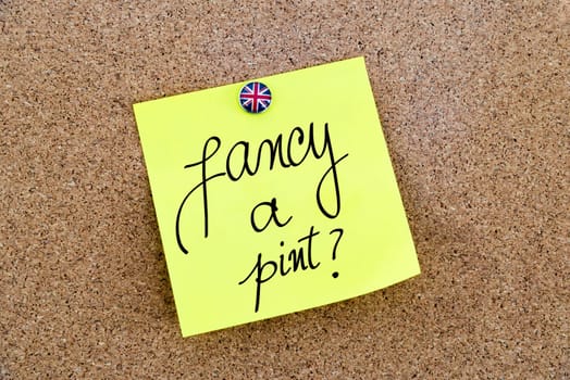 Yellow paper note pinned on cork board with Great Britain flag thumbtack, written text Fancy A Pint ?, British Business concept