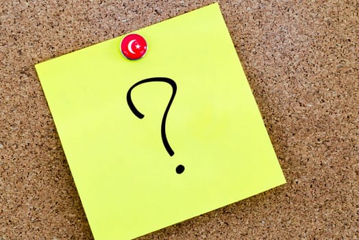 Question mark over yellow paper note pinned on cork board
