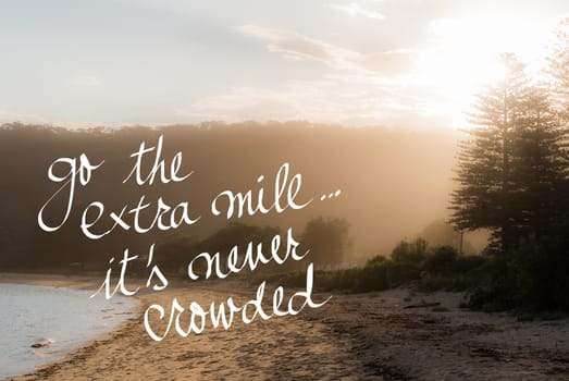 Go The Extra Mile Its Never Crowded message. Handwritten motivational text over sunset calm sunny beach background with vintage filter applied