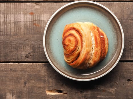 Delicious cinnamon pastry on a blue plate with space for text on the wooden background
