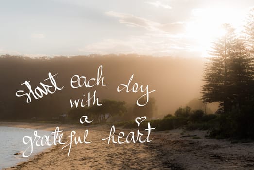 Start Each Day With A Greatful Heart message. Handwritten motivational text over sunset calm sunny beach background with vintage filter applied