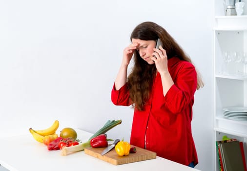 dark haired woman with red shirt in the kitchen is calling