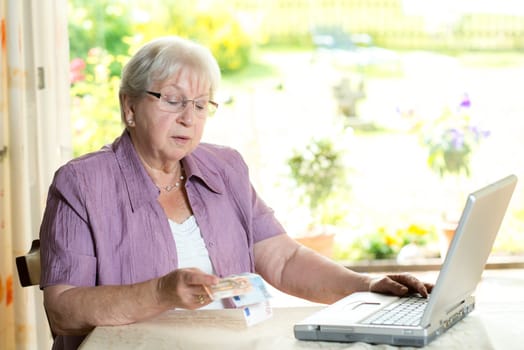 female senior with money in hand using computer at home