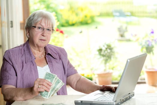 female senior with money in hand using computer at home