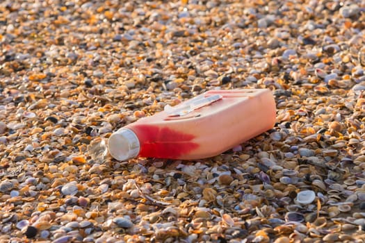 Plastic bottles of engine oil on the beach is strewn with small colorful sea shells