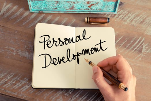 Handwritten text Personal Development as concept image. Retro effect and toned image of a woman hand writing a note with fountain pen on a notebook.