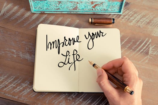 Handwritten text Improve Your Life as concept image. Retro effect and toned image of a woman hand writing a note with fountain pen on a notebook.