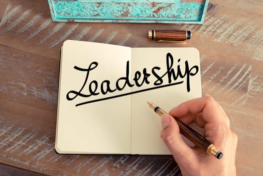 Handwritten text LeaderShip as concept image. Retro effect and toned image of a woman hand writing a note with fountain pen on a notebook.
