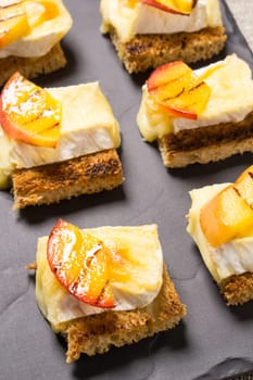 canapes, Appetizer with grilled brie and nectarine plated on a slate dish