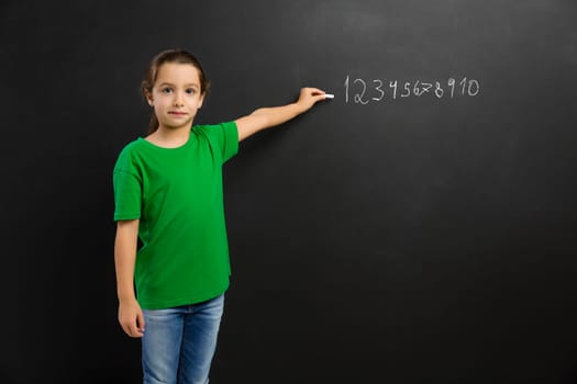 Smart little girl writing in a blackboard, with copy space