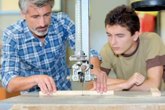 Carpenter using a bench saw, apprentice watching