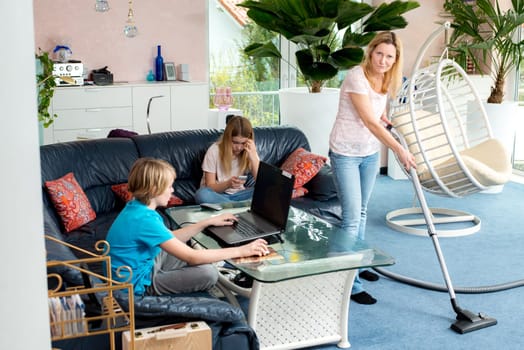 boy playing with computer, his sister using smartphone at home and mother doing homework