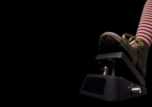 Horizontal side view of a show pressing a rock music pedal on black background