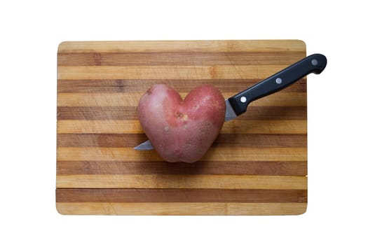 horizontal top view of a heart shaped potato on a wood cutting board with a kitchen knife going through it
