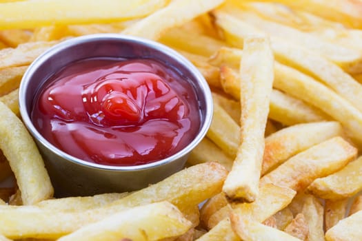 Close up shot of french fries surrounding cup of ketchup.