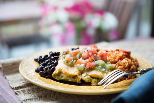 Vegetarian tamale dinner with black beans and rice topped with pico de gallo and salsa verde.