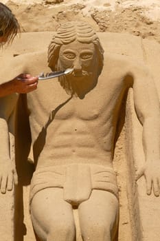 Young Man Working on Sand Sculpture of Jesus in Cadiz, Spain.