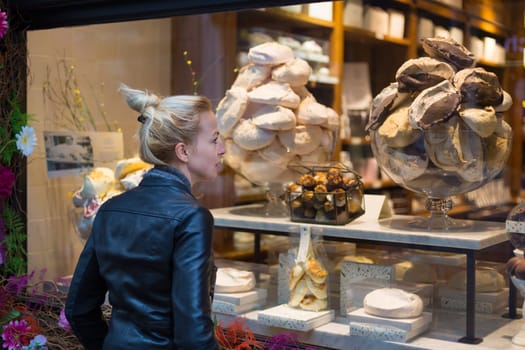 Lady window shopping in front of sinfully expensive chocolate boutique store dispaly window. Customer woman in shopping street, looking at window, outdoor.