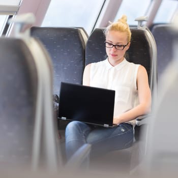 Businesswoman sitting and traveling by train working on laptop. Business travel concept.