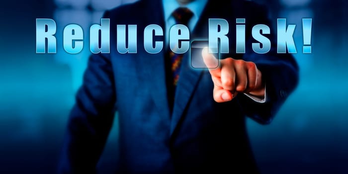 Corporate Manager is pressing Reduce Risk! on an interactive touch screen. Business objective concept, call to action, motivational metaphor and professional advice. Torso shot of man in blue suit.