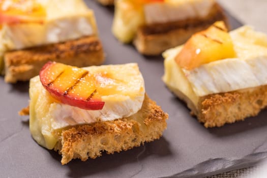 canapes, Appetizer with grilled brie and nectarine plated on a slate dish