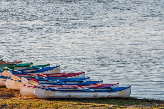Several kayaks lined up, one next to the other, on the river bank and ready for the adventures ahead.