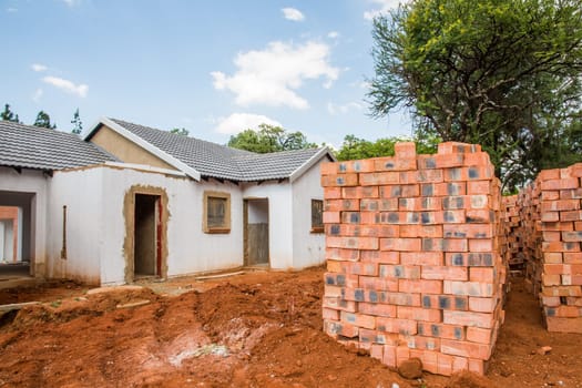 Building material stacked next to the imcomplete house that it is intended for.