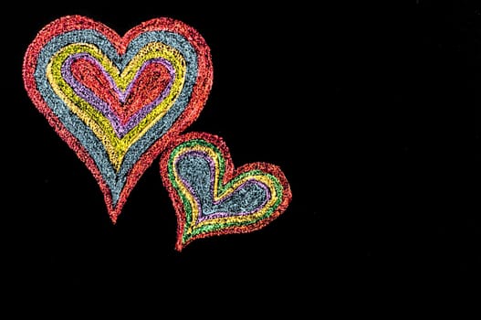 Conceptual image of love, with two vivid color shape hearts close one to each other .Vintage hand drawing on blackboard, isolated on black background, love concept, copy space available