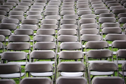 Parallel arranged empty rows of folding chairs on a meadow before a concert.