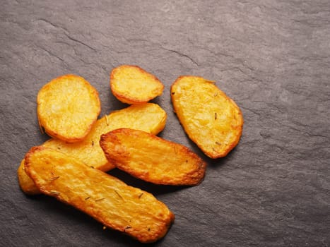 Roasted potato wedges with rosemary and thyme on a dark slate background with space for text