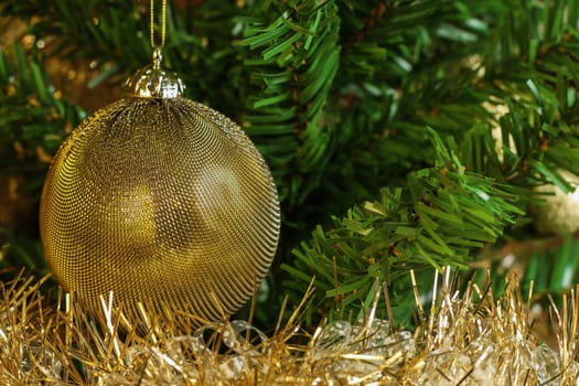 Horizontal image of the detail of golden decoration on the christmas tree with gold chain. Gold and green colours